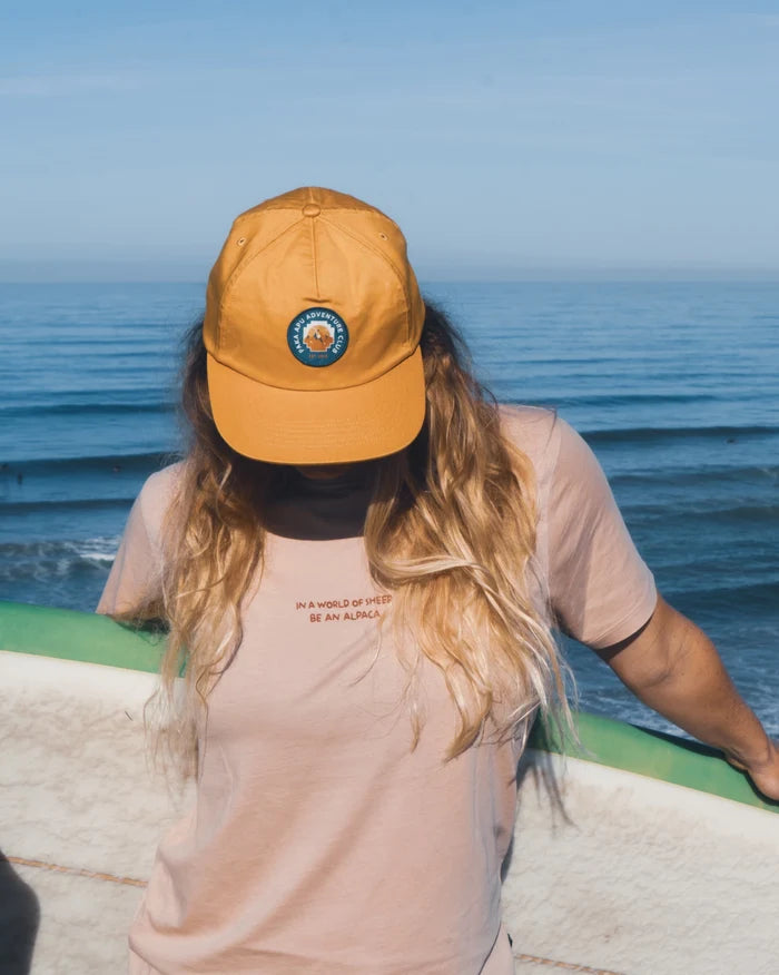 Woman Wearing Harvest Gold Adventure Hat with Patch While Holding Surfboard in Front of Ocean – PAKA Apparel