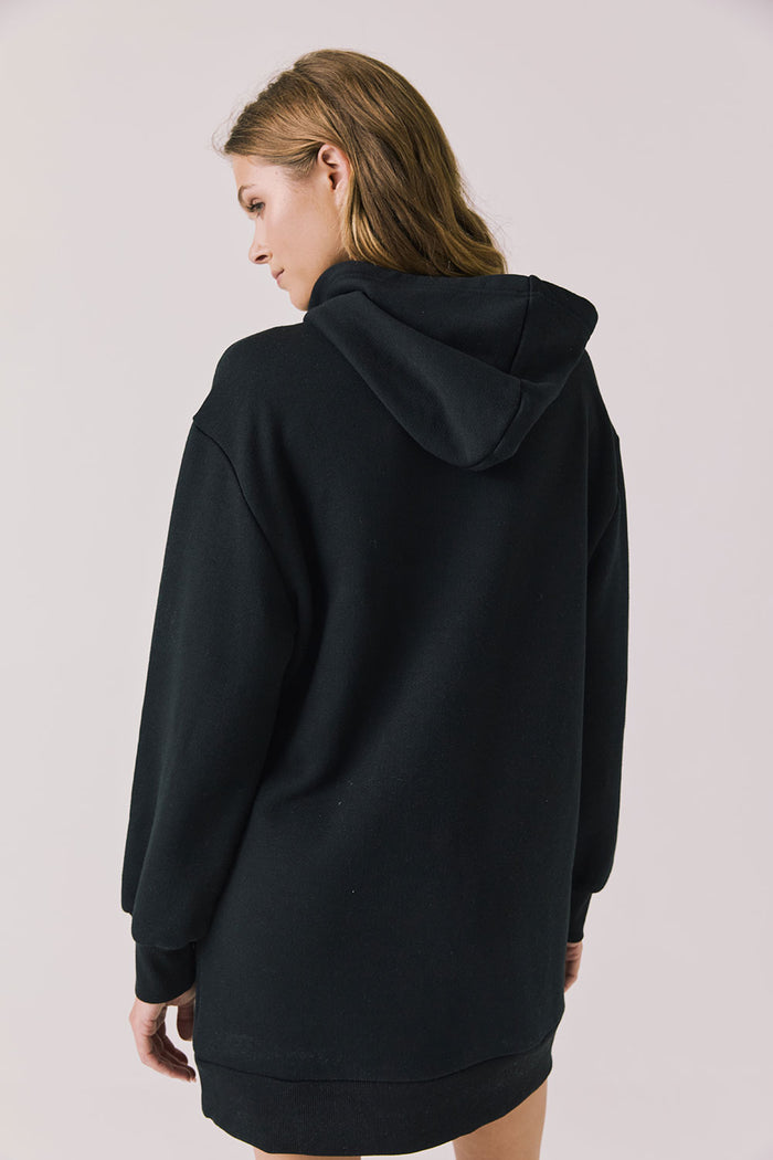 Back view of woman wearing Chaser Aster True Black Hoodie Dress on a plain background