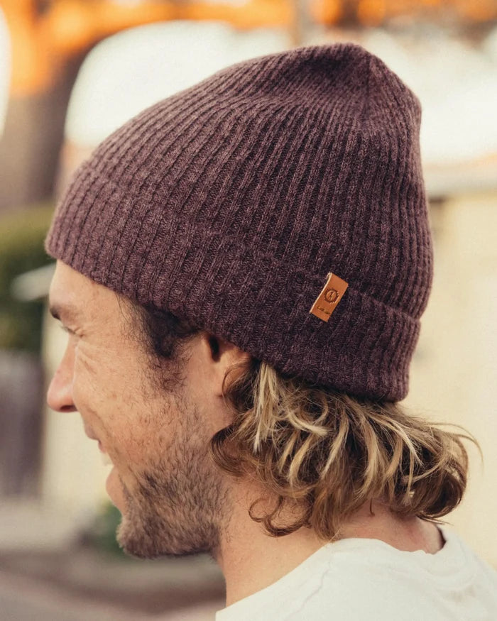 Side view of Cozy Marled Beanie in raisin marl on a model showing rib knit texture, folded cuff, and leather logo tab