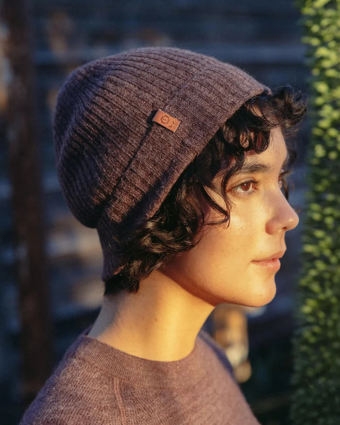 Right-side profile of Cozy Marled Beanie in Raisin Marl showing ribbed knit texture and leather logo tab on model outdoors