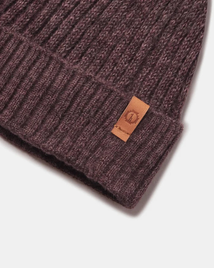 Close-up of Raisin Marl beanie showing ribbed cuff, fuzzy alpaca-blend knit and leather logo tab on light gray