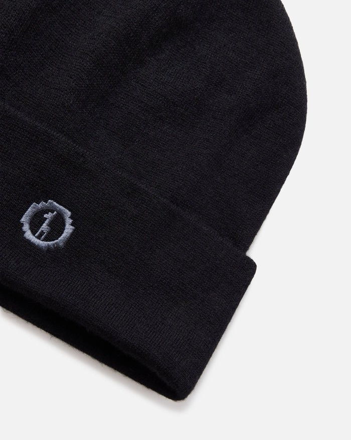 Angled close-up of black cuffed beanie showcasing embroidered PAKA logo on alpaca wool cuff against light gray background