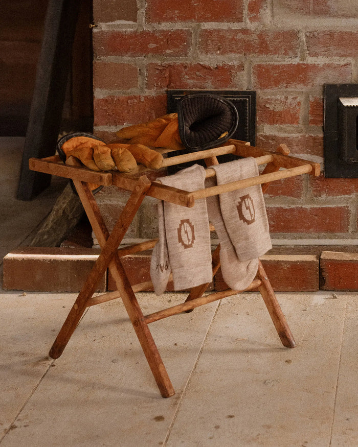 Beige alpaca crew socks draped over a small wooden folding rack beside a brick fireplace with leather gloves on top