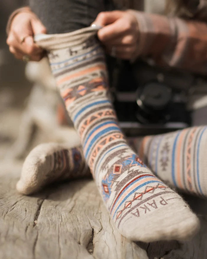 Close-up of Inca crew socks showcasing multicolor pattern and PAKA on the toe on a wooden log
