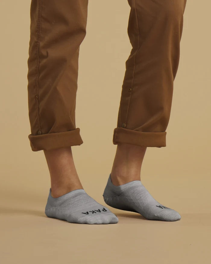 Angled front view of Essential No Show socks in light gray with low profile and PAKA logo on a beige background