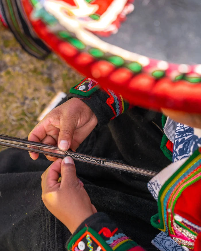 Quechua artisan weaving a handwoven alpaca Inca-pattern bracelet, close-up on hands and colorful traditional clothing