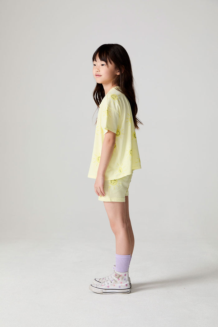 Side view of a girl wearing the Chaser Happy Happy Shorts and matching yellow shorts on a neutral background