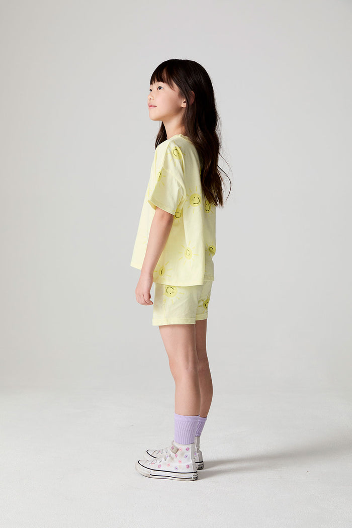 Side view of a girl wearing the Chaser Happy Happy Tee on a neutral background with arms at her sides