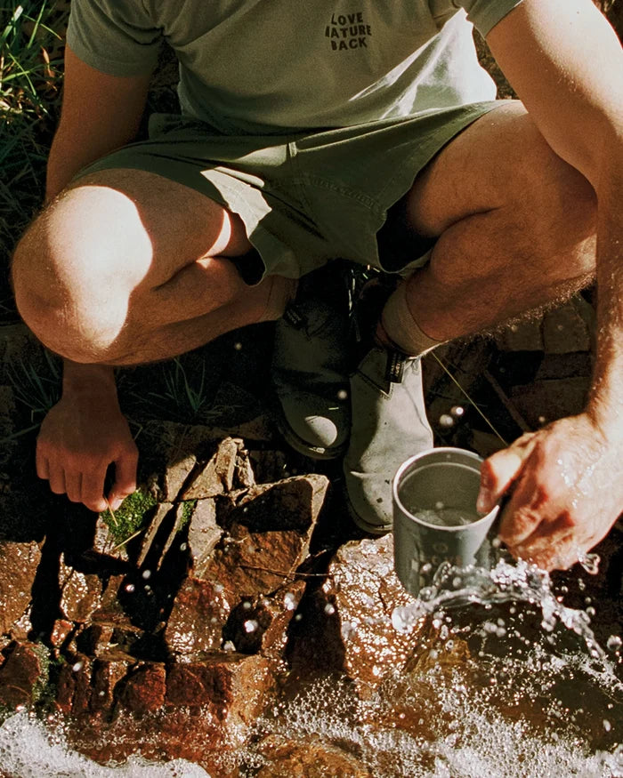 Person squatting by a stream, washing something in a cup.
