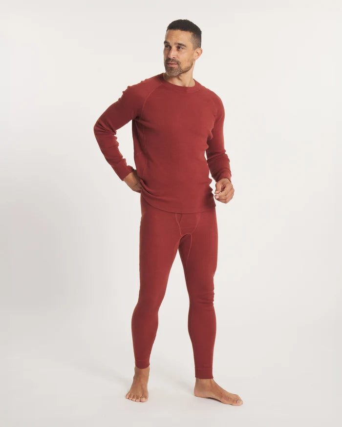 Three-quarter view of men’s alpaca baselayer thermal bottoms in clay red showing slim full-length fit on a light studio background