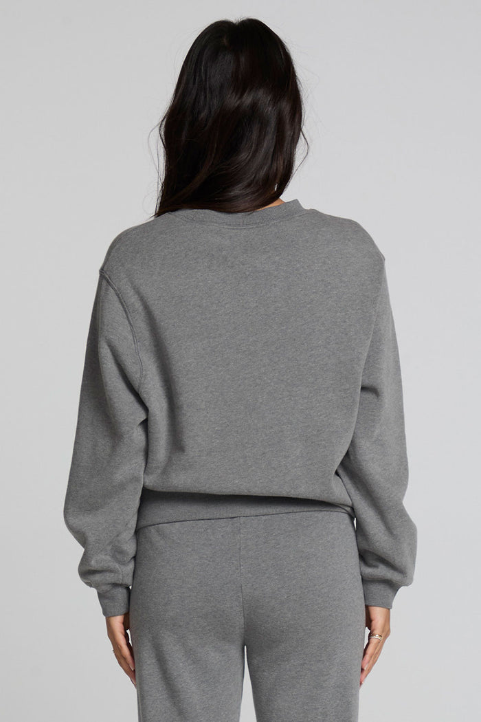 Back view of a woman wearing the Chaser  Mini Star Glaze Sweatshirt on a neutral background with arms at sides in matching sweatpants