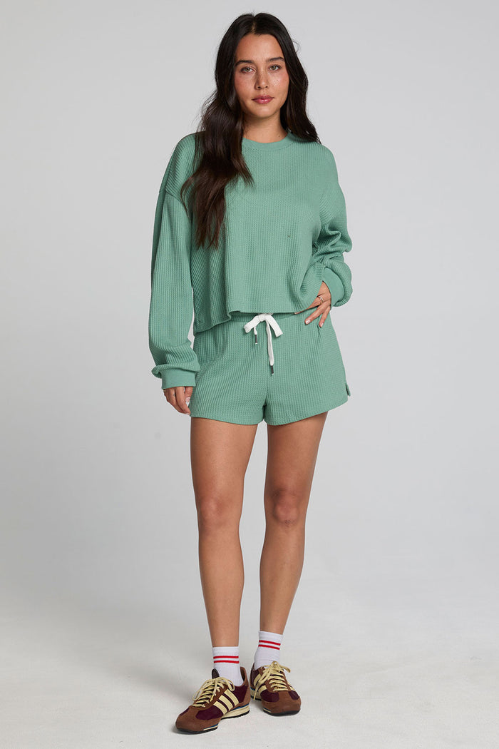 Full body front view of a woman wearing the Chaser Suzzans Verdelle Sweatshirt on a neutral background with matching green shorts