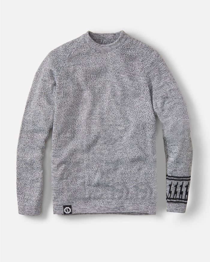 Front view of The Costa sweater showing gray sherpa fleece texture, patterned cuff, and logo patch on light background