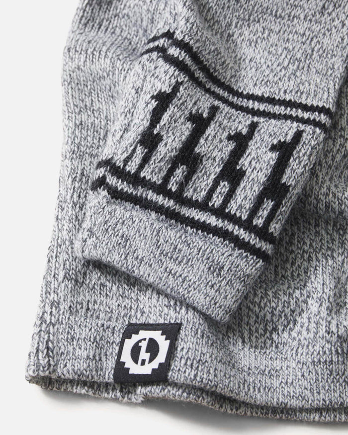Close-up of Costa crew sweater sleeve showing marled light-grey alpaca knit, black geometric cuff pattern, and woven brand label on white background