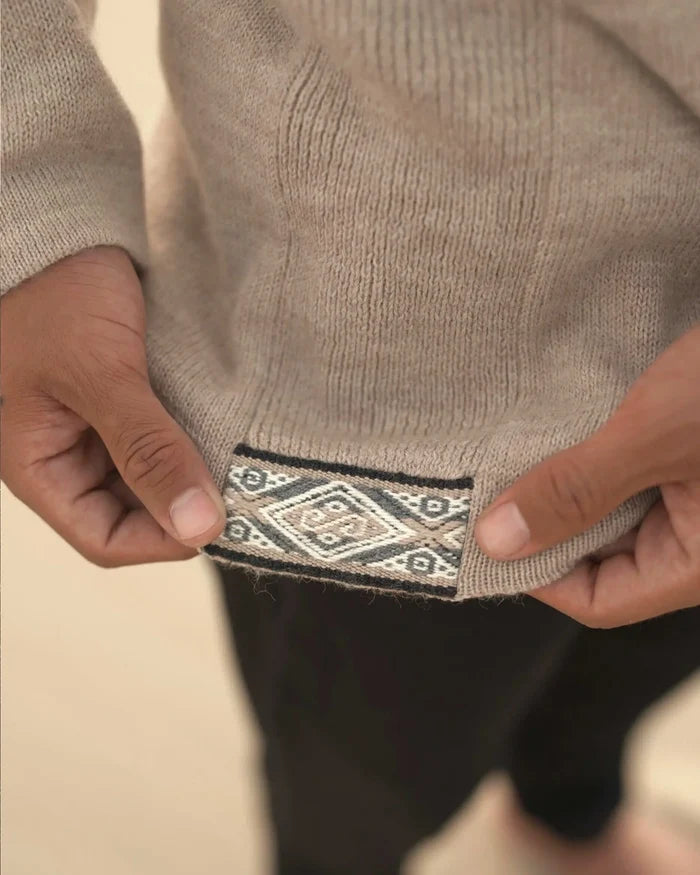 Close-up of The Hoodie hem showing woven Inca side tag held by hands against blurred neutral background