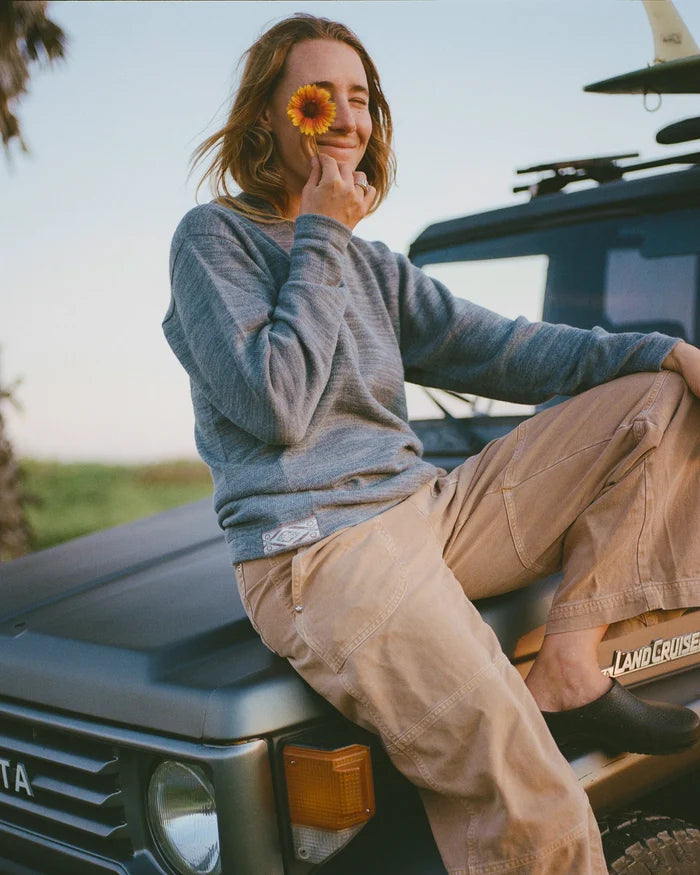 A woman sitting on the hood of a Land Rover holding a sunflower while wearing PAKA's The Hoodie in Bluestone