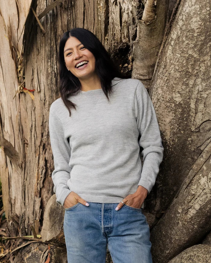 Front view of The Hoodie alpaca hoodie in light grey showing relaxed fit on model leaning against a tree background