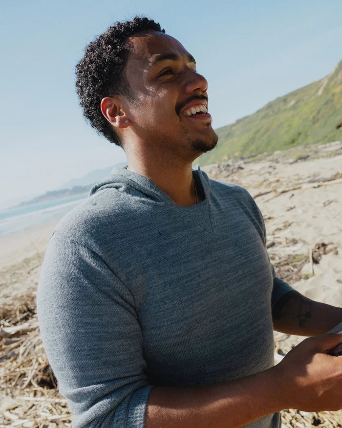 Man wearing PAKA's The Hoodie in Bluestone smiling on the beach