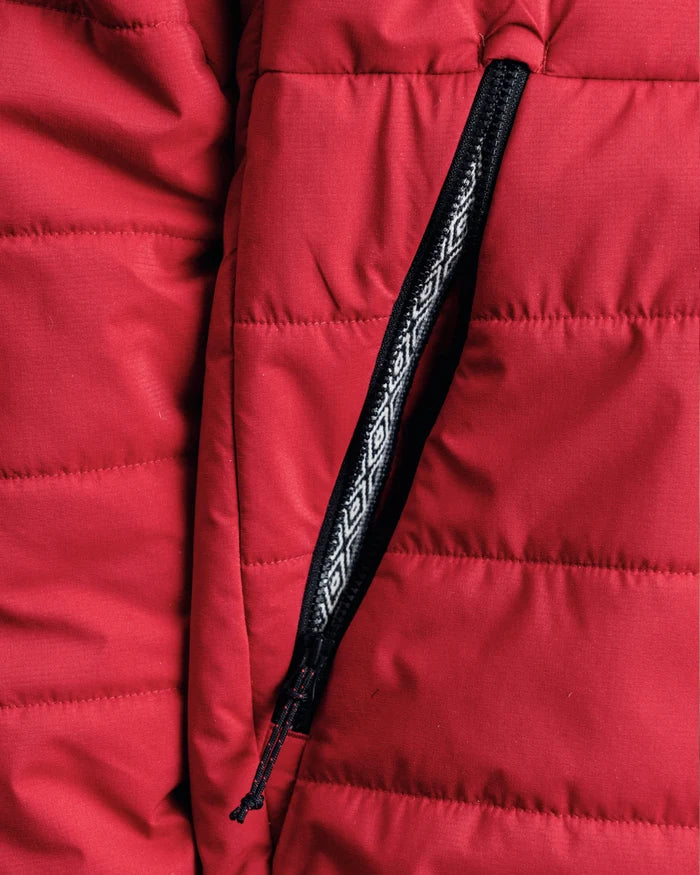 Close-up of The Huascarán Jacket showing red recycled nylon quilting and zippered pocket with black patterned pull tab