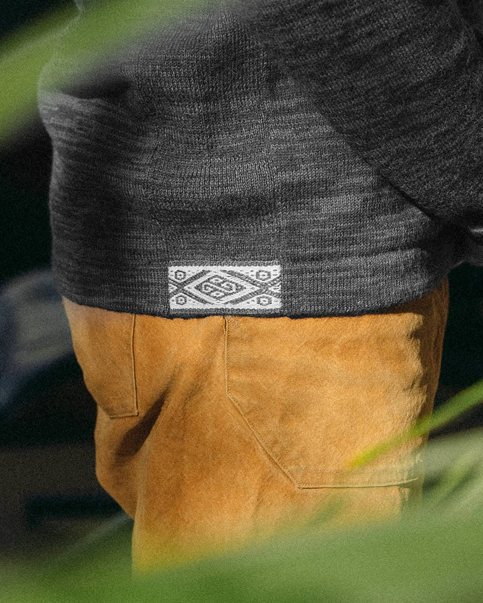 Close-up of The Quarter Zip charcoal hem showcasing woven logo tag and alpaca knit texture against tan pants background