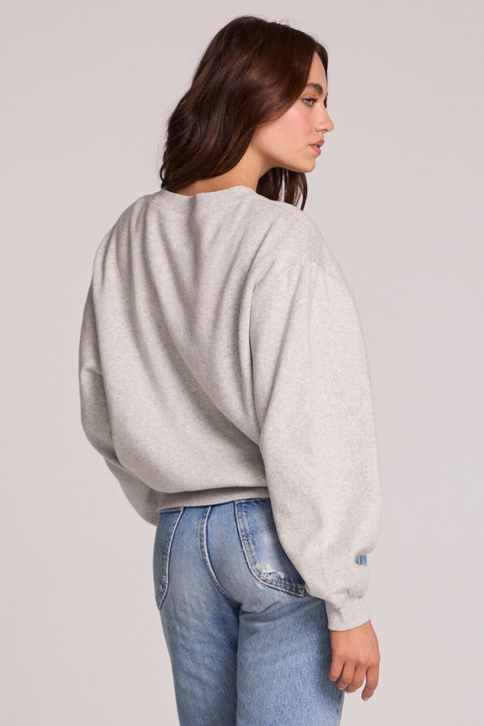 Back view of a woman wearing the Chaser The Rolling Stones Long Sleeve Tee on a neutral background with hand on one hip and jeans