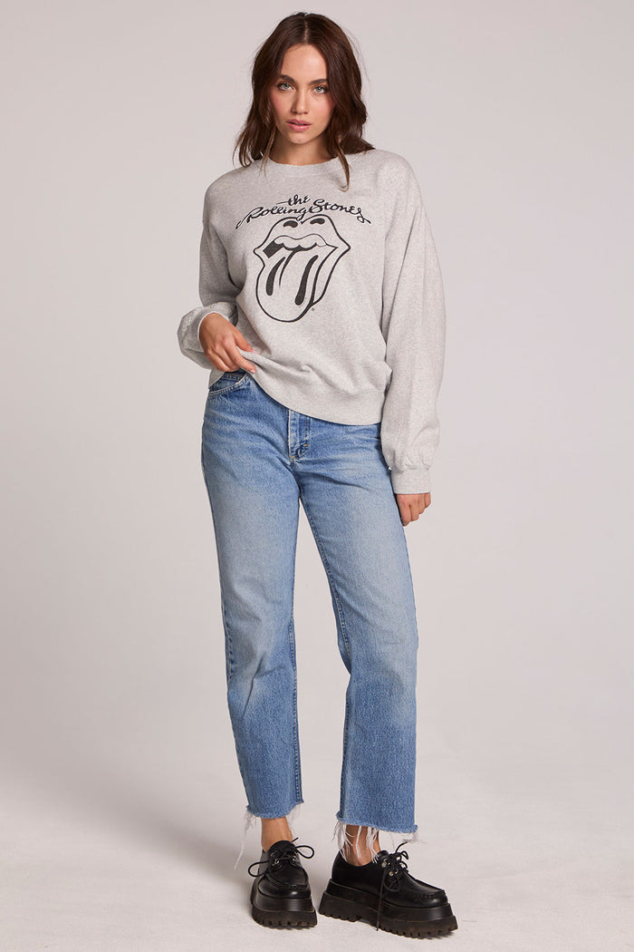Full body view of a woman wearing the Chaser The Rolling Stones Long Sleeve Tee on a neutral background with hand on one hip and blue jeans