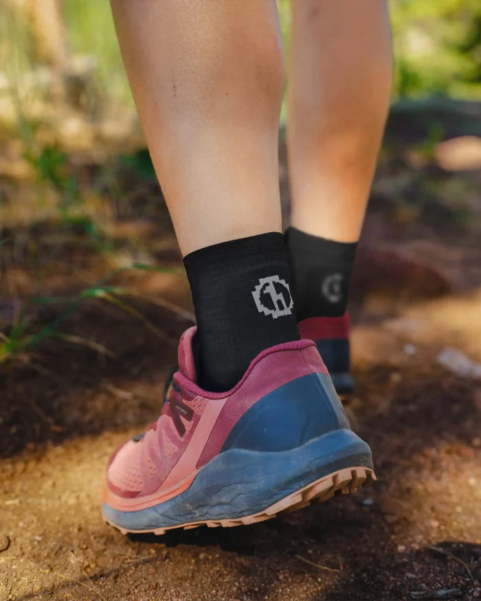 Back view of a hiker wearing black Trail 1/4 crew socks on a dirt trail with pink hiking shoes