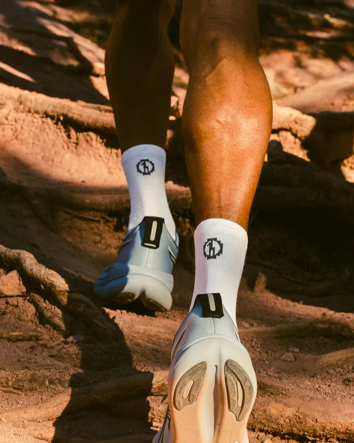 Rear view of Trail 3/4 Crew socks in white showcasing 3/4 crew height and PAKA cuff logo on a model walking on a rocky trail