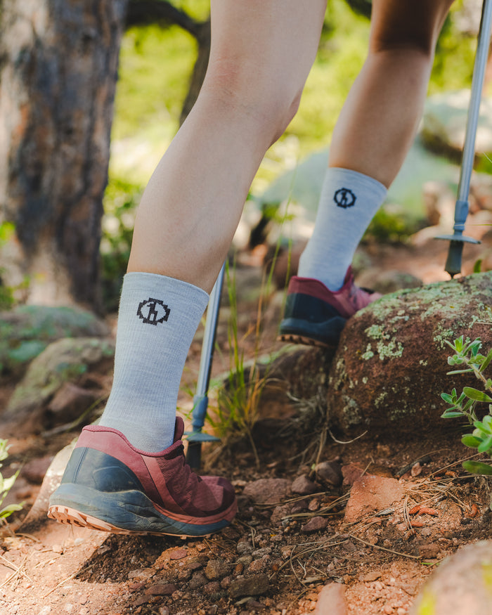 Rear view of Trail Crew alpaca hiking socks in light gray on model showing crew height and logo on a forest trail