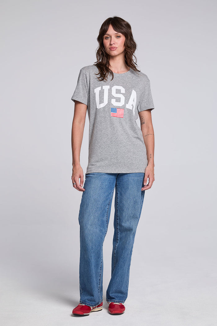 Model wearing Chaser USA Flag Oversized Tee in Streaky Grey styled with loose straight leg jeans and red sneakers