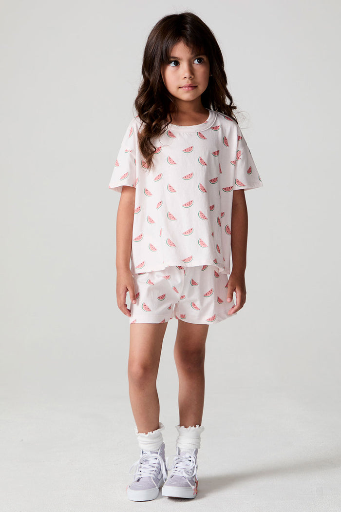 Full body side front view of a girl wearing the Chaser Watermelon All Over Tee on a neutral background with arms at sides