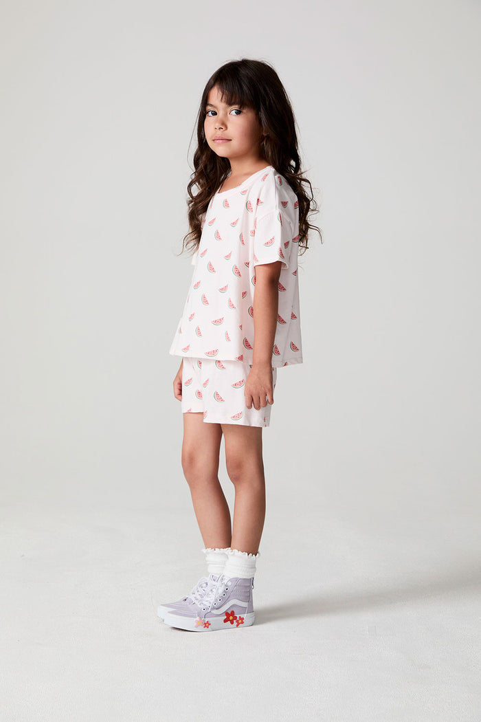 Full body side angle view of a girl wearing the Chaser Watermelon All Over Tee on a neutral background