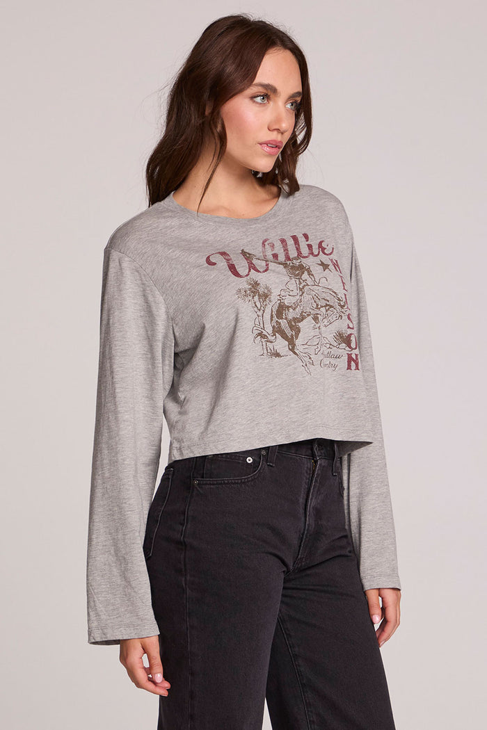 Side angle view of a woman wearing the Chaser Willie Nelson Horseback Long Sleeve on a neutral background with arms at sides and pants