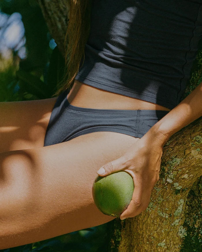 Side view of Women’s Essential Bikini Brief on model showcasing lower-profile cut and smooth breathable alpaca fabric with tree trunk background