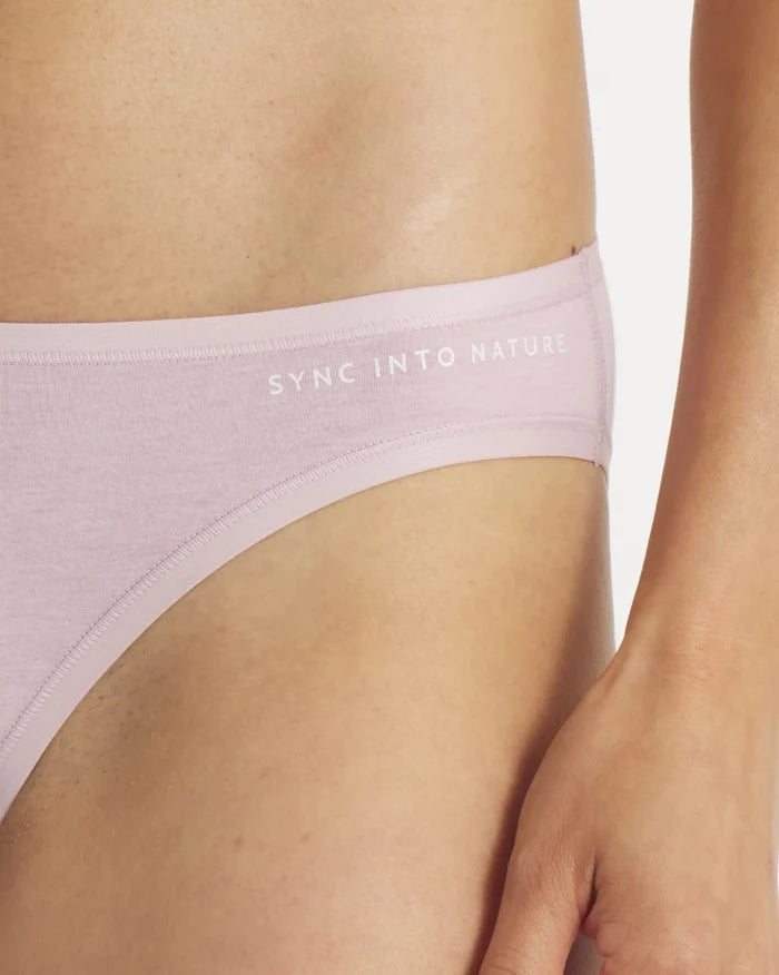Close-up of lilac Women’s Essential Bikini Brief low-rise waistband with ‘SYNC INTO NATURE’ print on hip against white