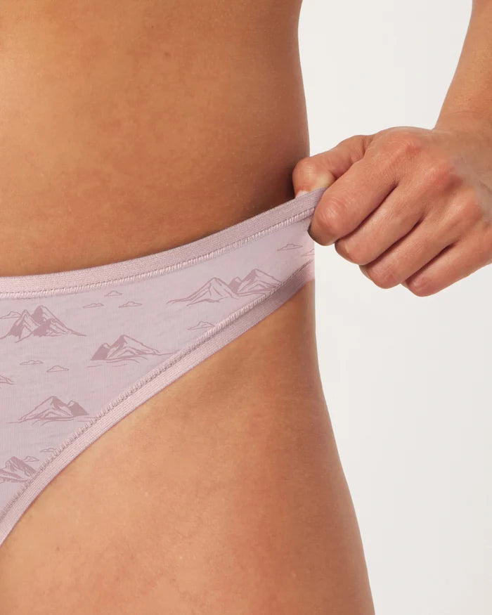 Close-up side view of Women’s Essential Printed Bikini Brief in Smokey Lavender showing mountain print and elastic waistband being stretched by model against white background