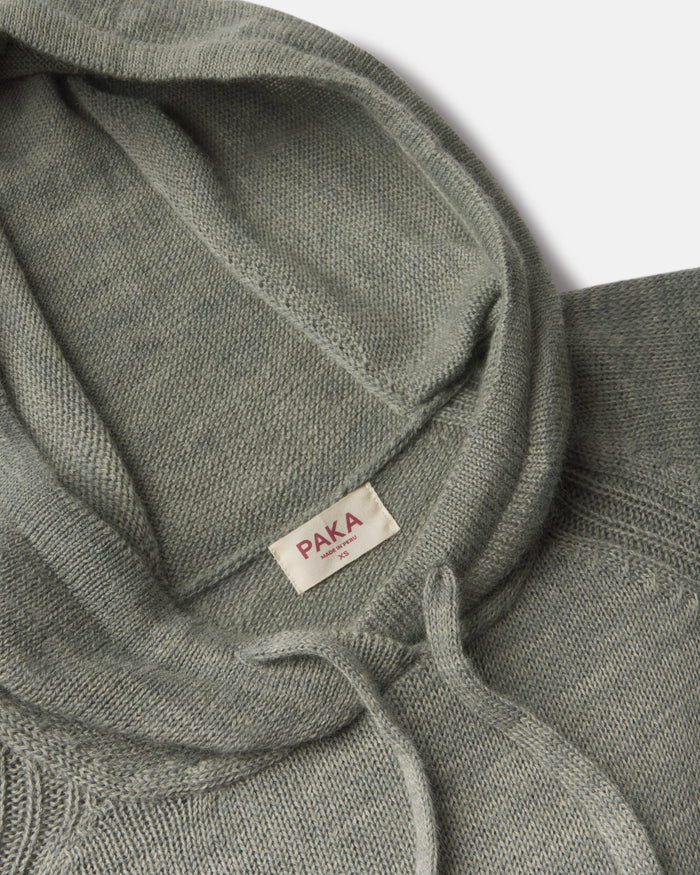 Close up overhead of women’s alpaca hoodie showing hood interior, drawstring, PAKA label and soft sage green knit on light background