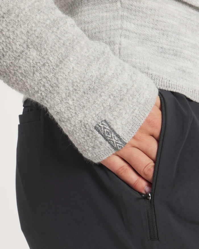 Close-up of a hand wearing the Women's Mountain Crew Sweater in Light Grey sleeve with a brand logo on a light gray background
